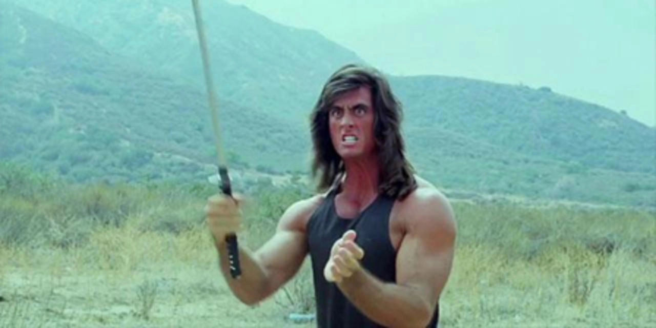 A man with a mullet and a maniacal face holding a sword in the middle of a field.
