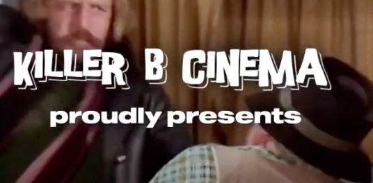 A screenshot from the trailer of a film.  There is easy-to-read text overlayed on top of the action in the background that reads 'Killer B Cinema proudly presents'.