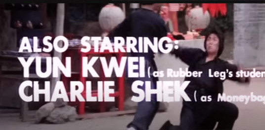 Two men fighting in the background with words overlayed on top that read 'Also Starring: Sun Kwei (as Rubber Legs student'), Charlier Shek (as Moneybags)'.  Like the previous screenshot, some of the text is hard to read since the white text sometimes blends into the light background of the ground.